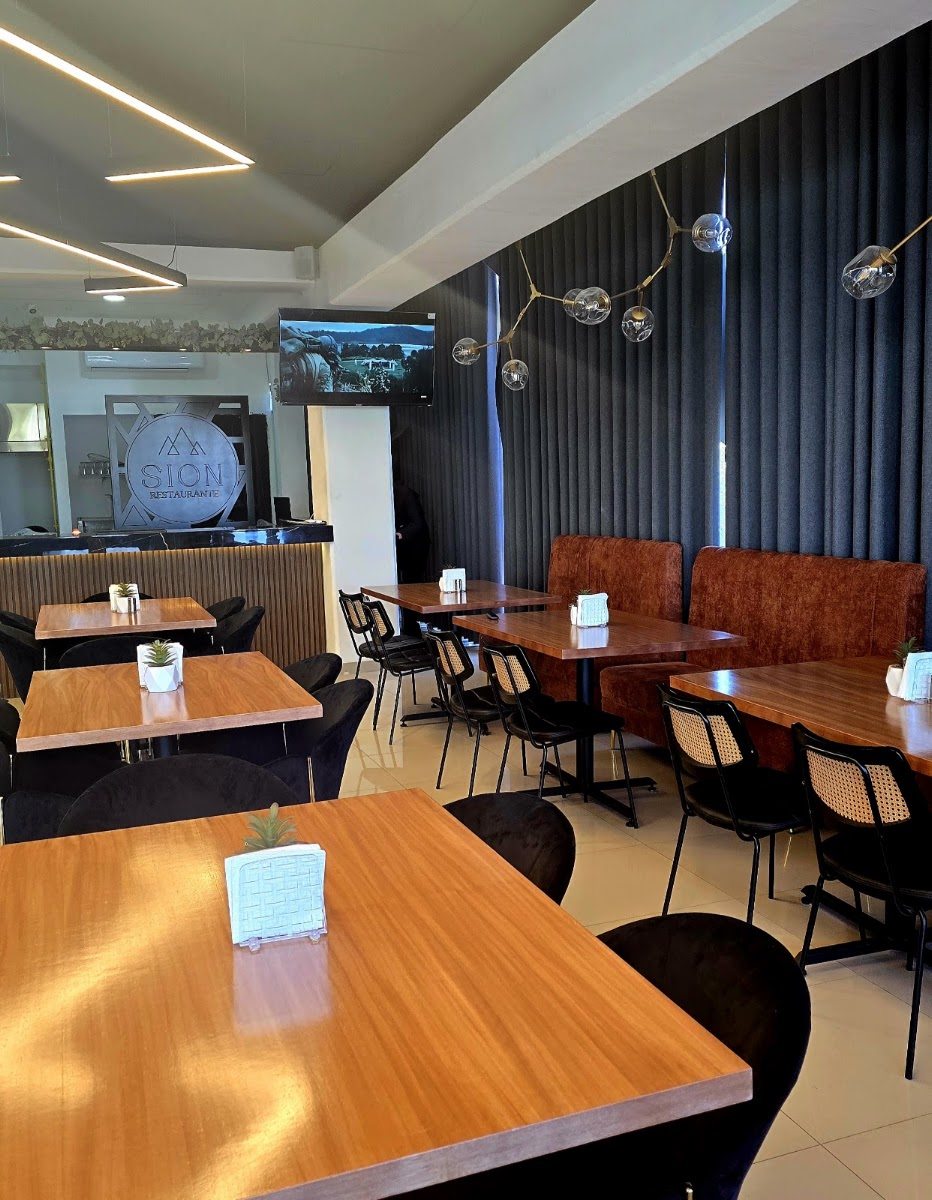 Salón de Sion Restaurante: mesas de madera, sillones color terracota, muro acanalado oscuro y una lámpara de brazos dorados